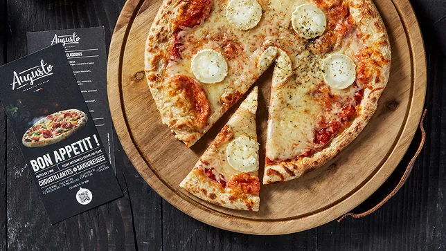 Une pizza au fromage de chèvre coupée sur une planche en bois, la carte posée à côté